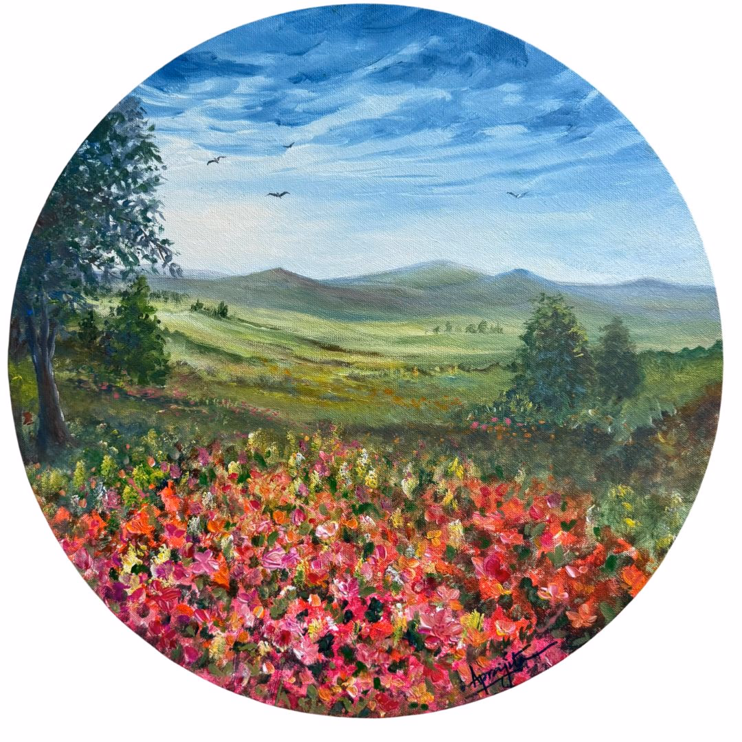 A circular acrylic painting titled 'A Meadow in Bloom' depicting a vibrant field of red and pink flowers in the foreground, rolling green hills in the middle ground, and distant blue mountains under a cloudy blue sky. A tree is on the left.
